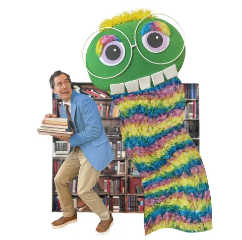 A photo depicting a man holding a stack of books standing beside a large bookworm puppet.